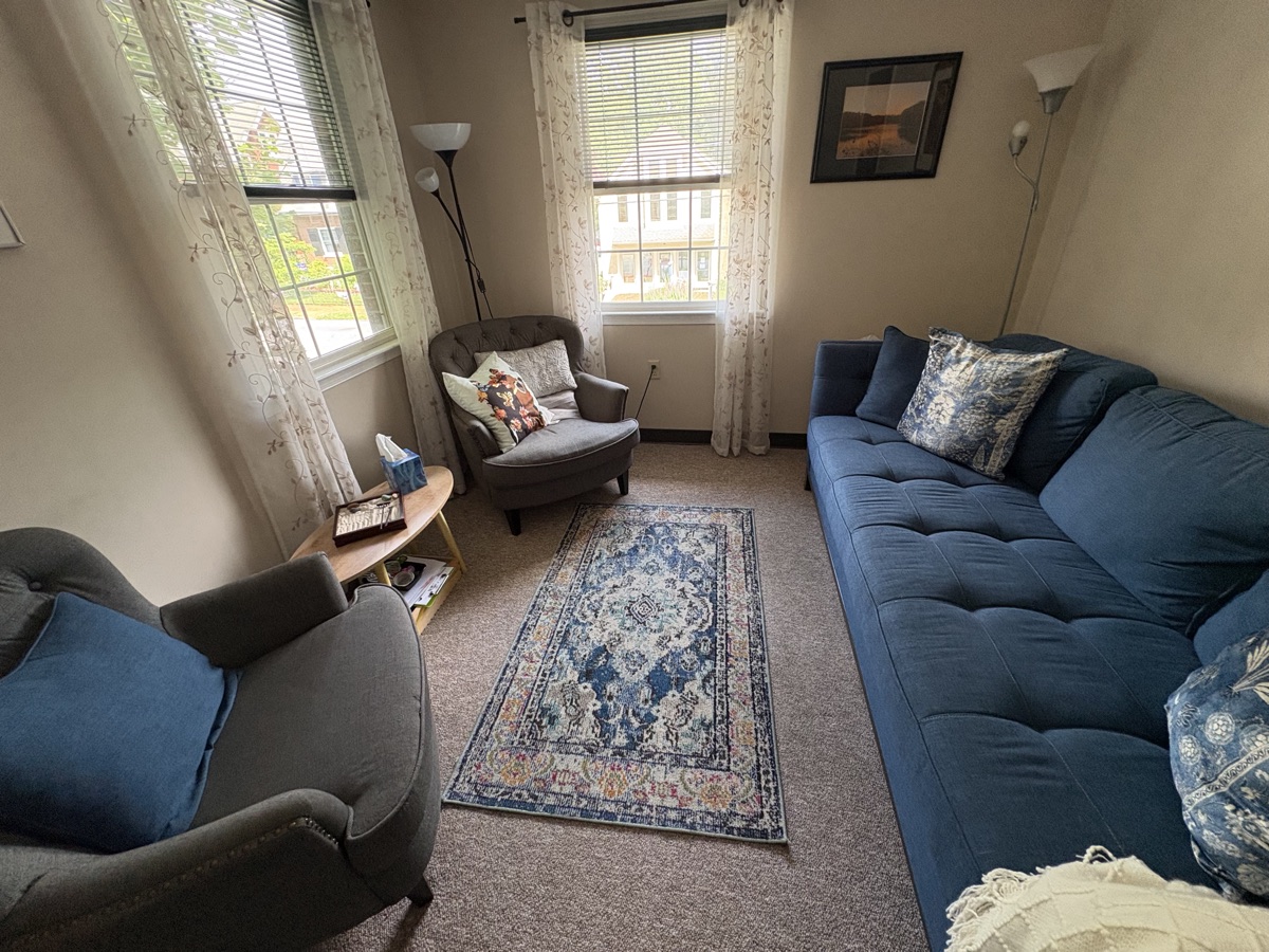 A bright therapy room with a comfortable sofa and large sunlit windows